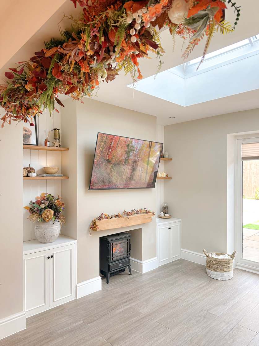 living room with hanging autumn garland, TV, forest backdrop, electric fireplace, muted earth tones