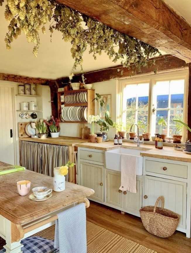 Kitchen with hanging bunches of dried hops, reclaimed wood cabinets, farmhouse sink, warm lighting.