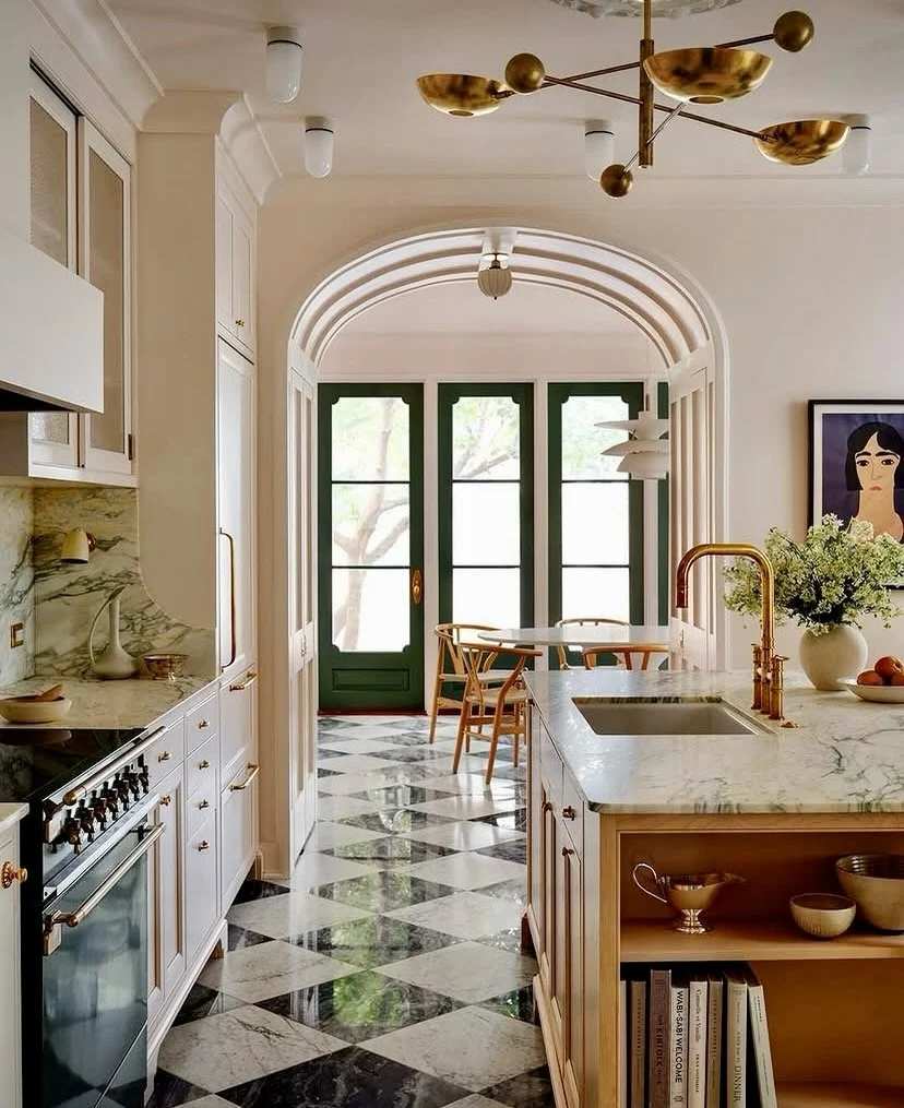Serene kitchen with ivory walls, sage green cabinets, white marble island, brass pendant lights, natural wood floor.