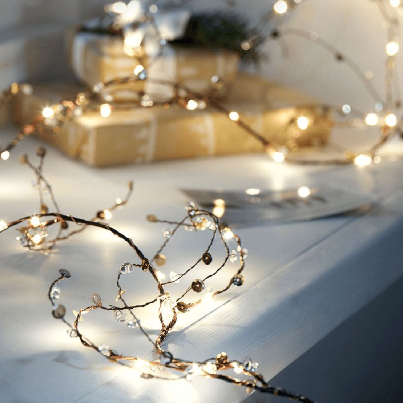 Modern living room wooden console table styled with illuminated jewelled twig garland and warm lighting