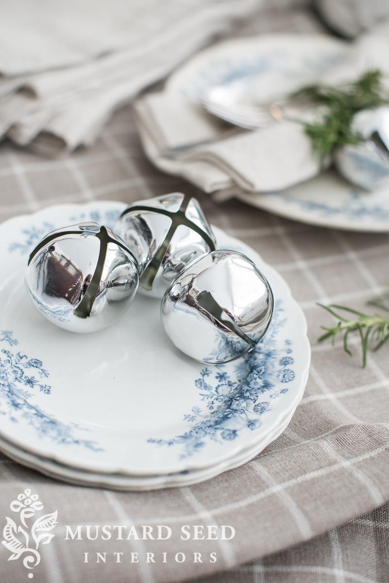 Festive dining room featuring white oak, linen napkins, silver jingle bell rings, and warm candlelight.