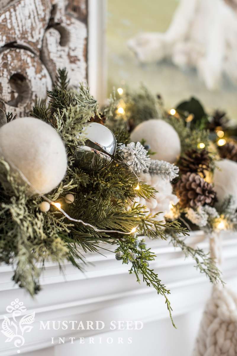 Living room fireplace mantel with rustic brass jingle bells, faux cedar garland, warm light.