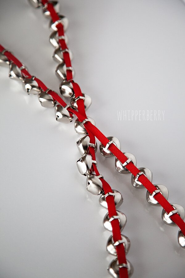 Traditional staircase banister with evergreen swag, mixed metallic jingle bells, silk ribbon, warm ambient light.