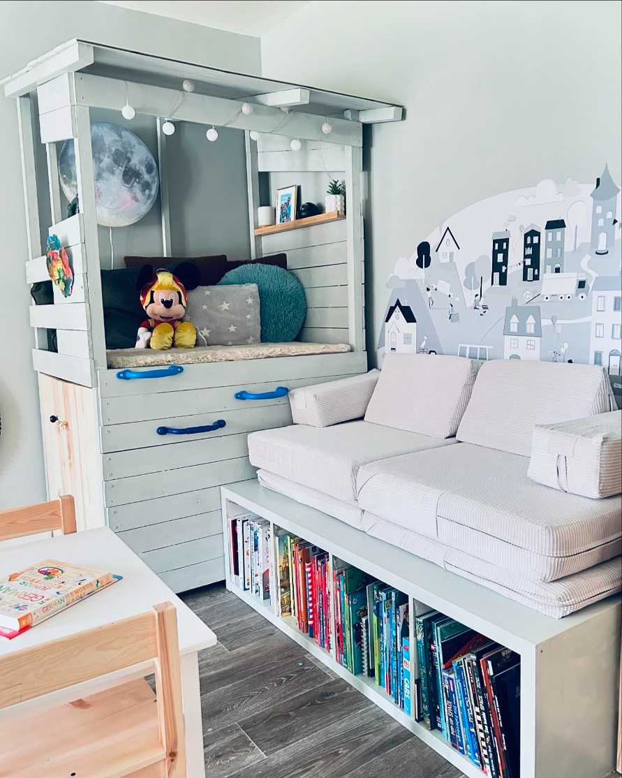 Wooden playhouse cubby bench, colorful cushions, string lights, low bookshelf, bright wall paint.