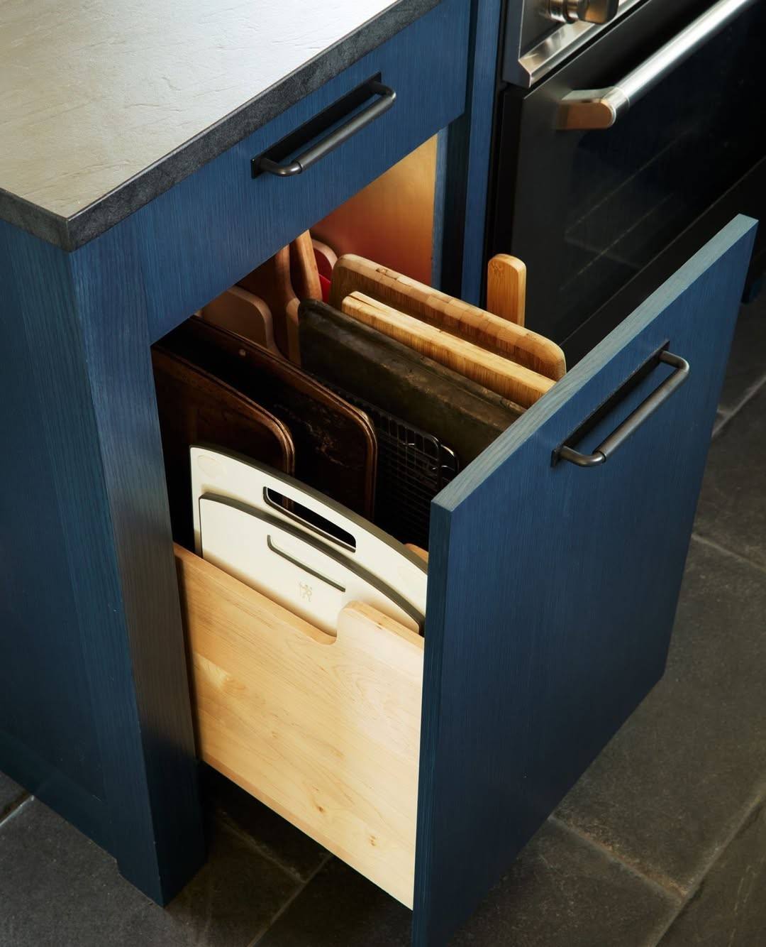 Navy blue kitchen island with oversized brass hardware in a bright, airy white kitchen space.