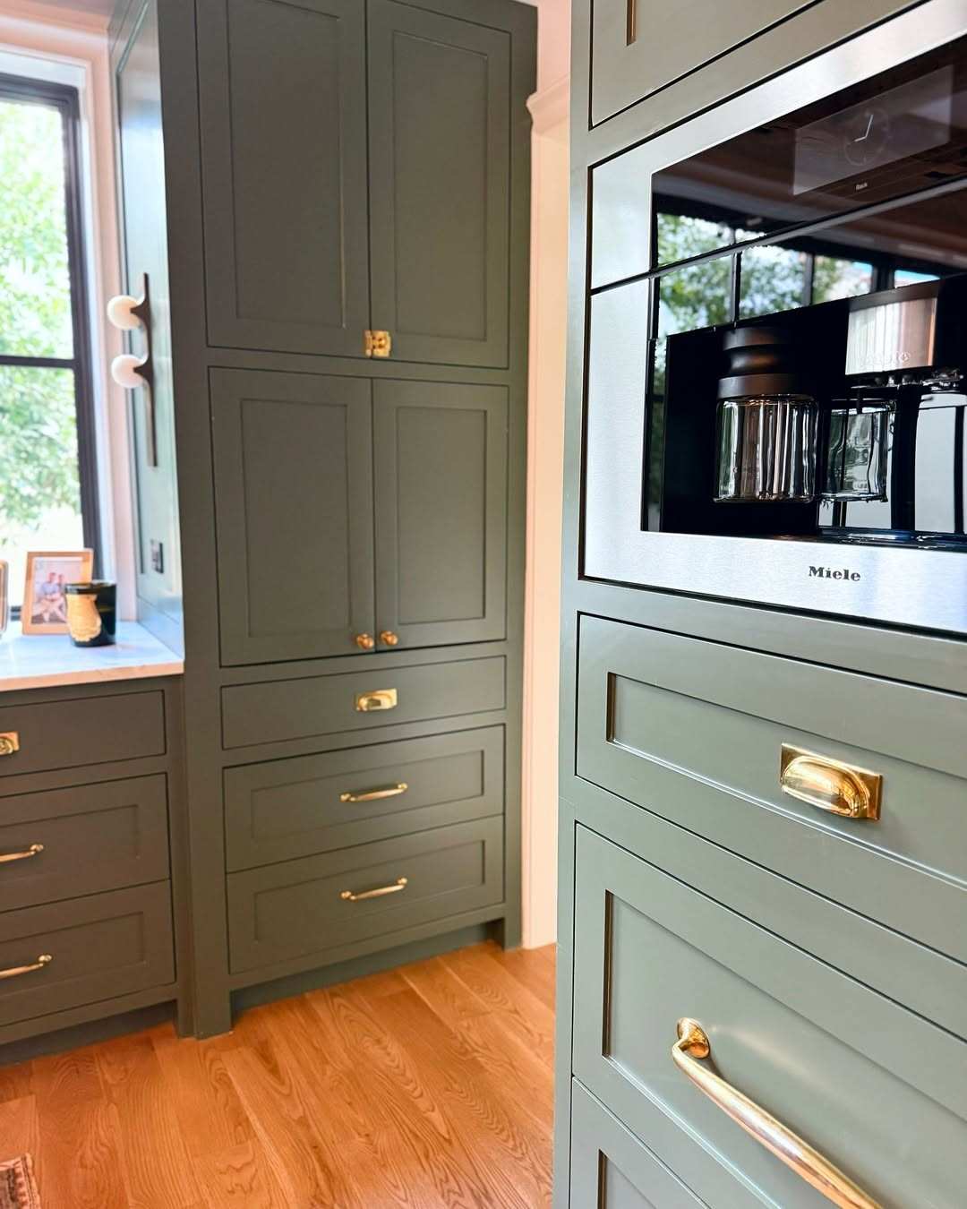 Deep forest green cabinets with matte brass hardware in a sophisticated kitchen interior.