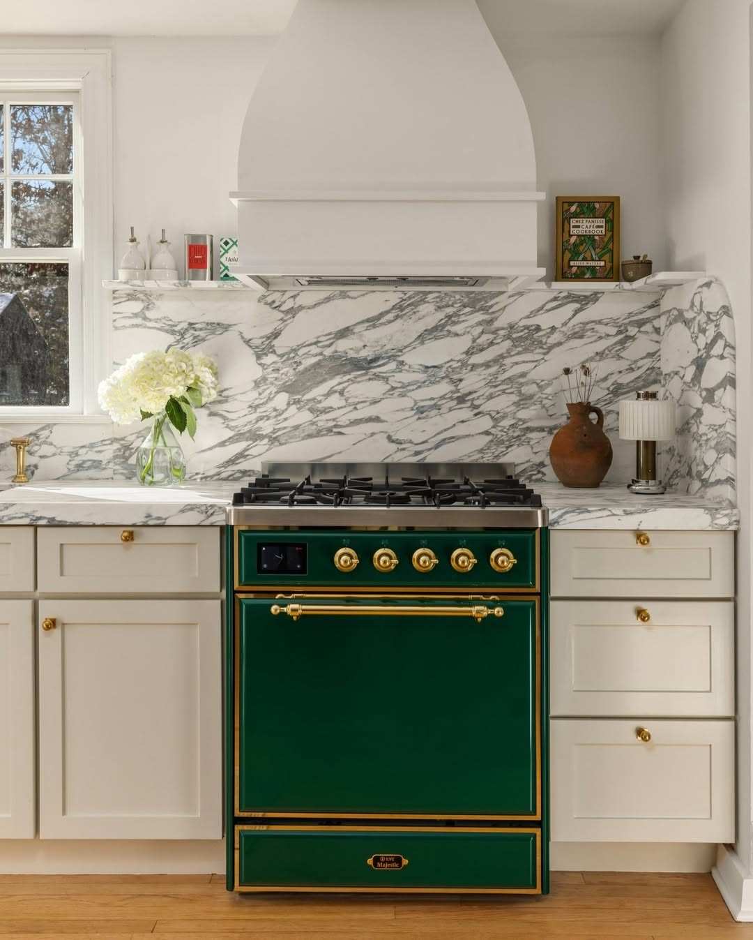Green kitchen featuring a range with gold-toned knobs and brass cabinet hardware.