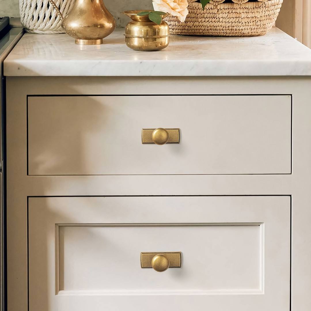 Detailed close-up view of elegant brass knobs installed on white kitchen drawers.