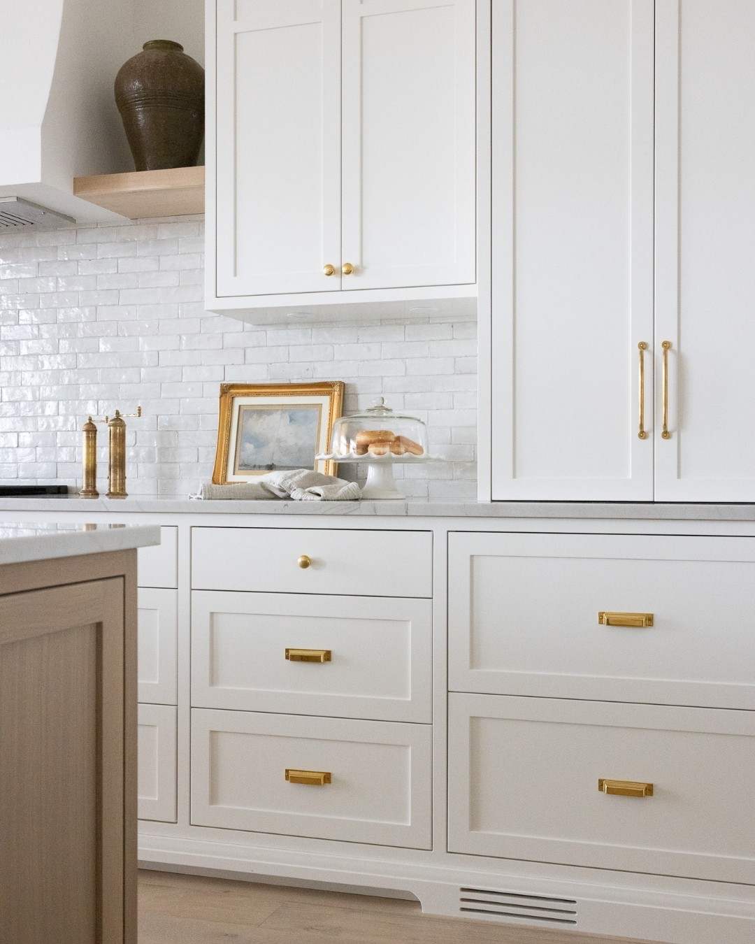 A classic white kitchen featuring traditional brass cabinet knobs throughout.