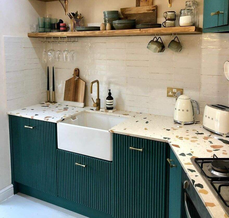 Kitchen featuring sage green cabinets, wood floating shelves, subway tile backsplash, and natural sunlight.
