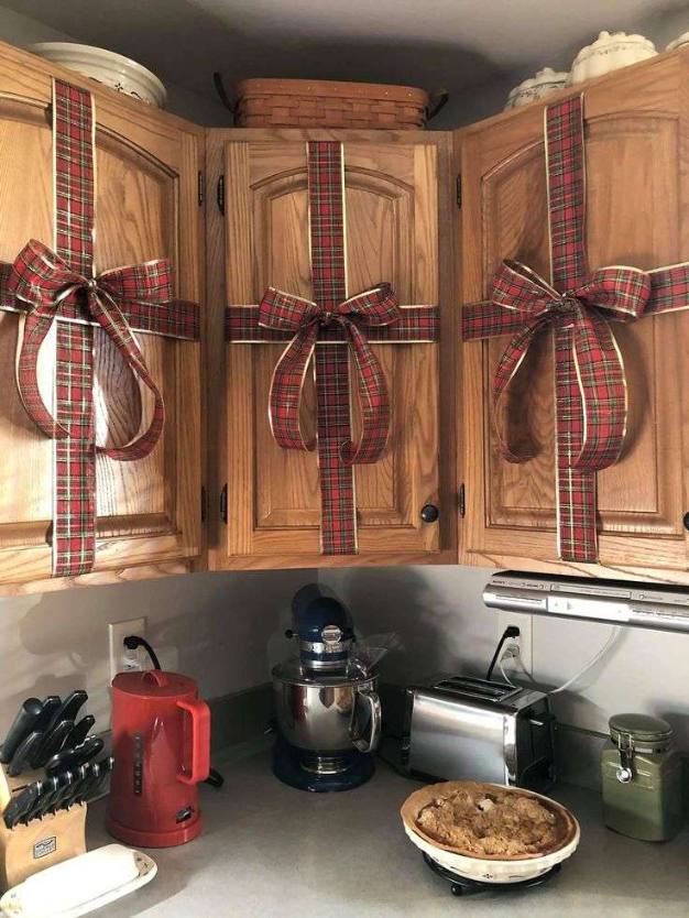Kitchen cabinets featuring a row of small red ribbon bows tied around each drawer front, complementing stainless steel handles.