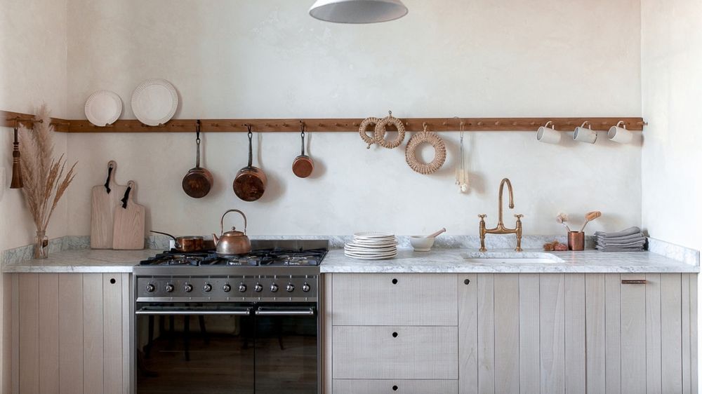 Kitchen with matte terracotta tile backsplash, cream shaker cabinets, and brass hardware lighting.