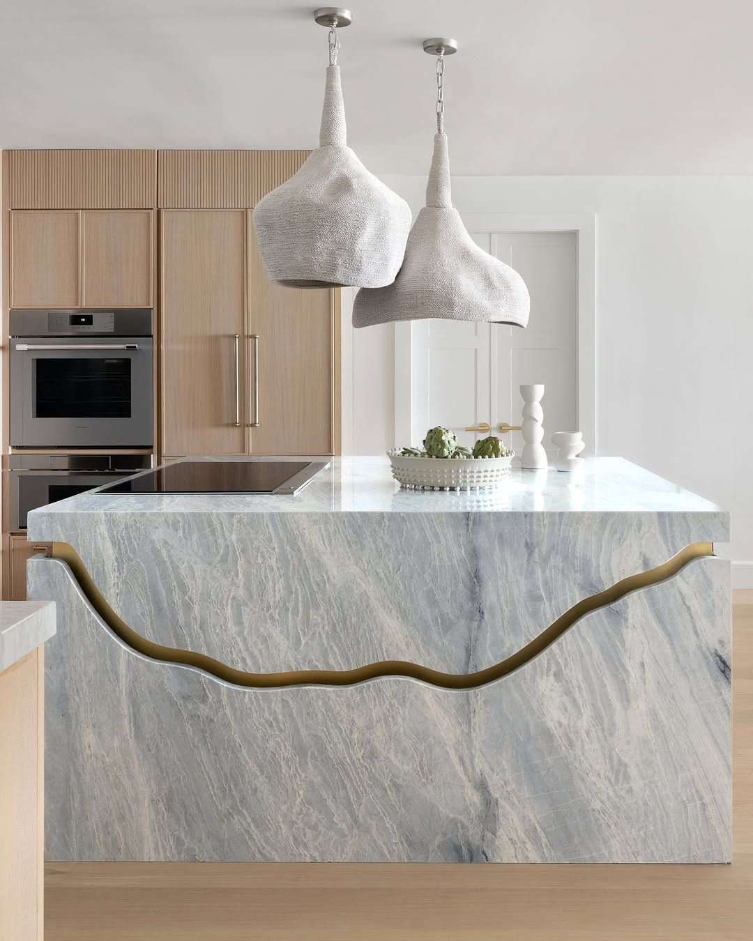 A minimalist all-white kitchen island with waterfall marble edges and hidden storage compartments.