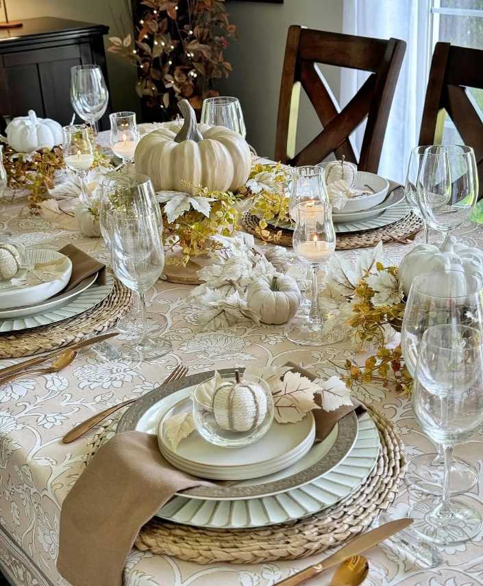Cozy dining nook, knit sweater textured pumpkins, champagne glassware, soft gray linens, dim lighting