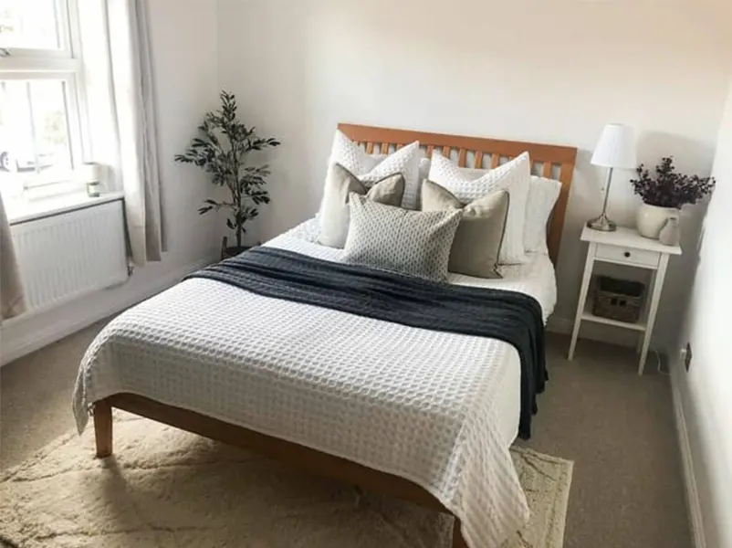 Bedroom with layered neutral bedding, bright window views, and soft natural lighting.