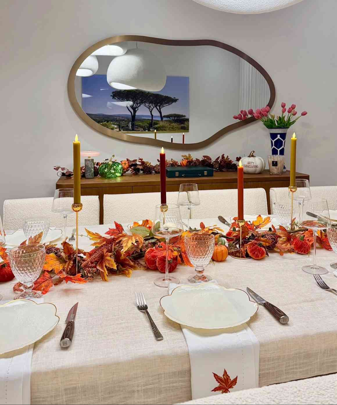 Dining room, leaf garland runner, velvet pumpkin décor, tall pillar candles, warm ambient lighting.