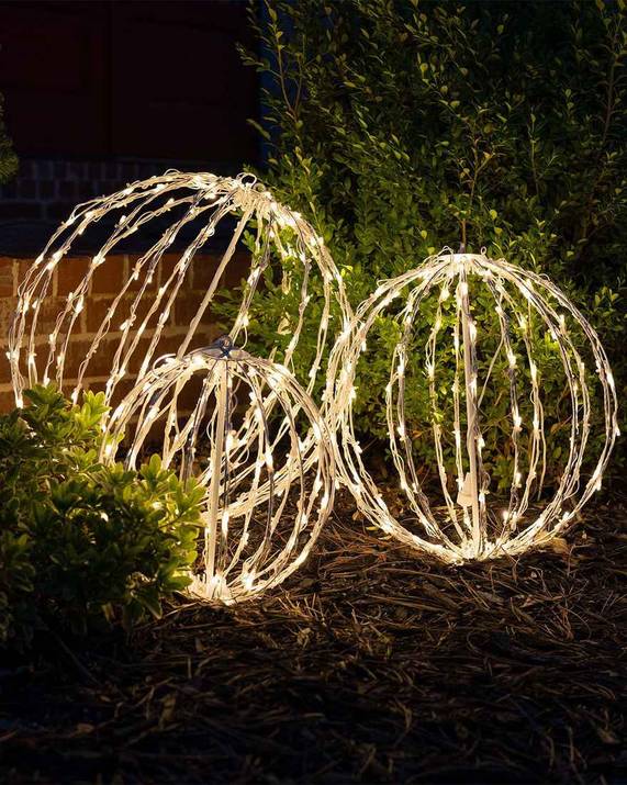 Clusters of glowing light balls placed in a snowy garden as outdoor christmas decorations.