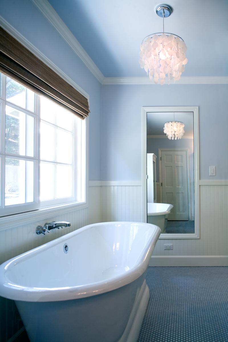 Light blue bathroom walls surrounding a sleek white freestanding bathtub with polished nickel hardware.