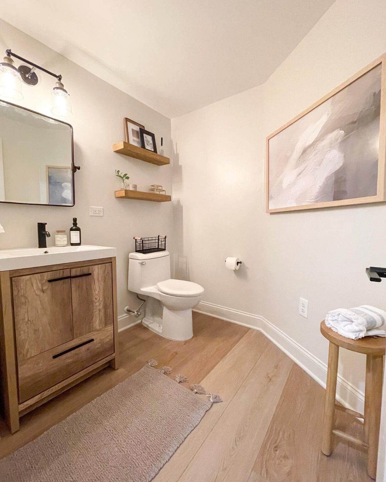 Half bathroom featuring light wood vanity, floating wooden shelves, white sink, natural light.