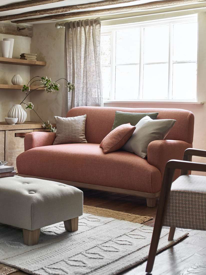 Farmhouse living room with natural burlap curtains, wooden beams, fireplace, cozy leather furniture.