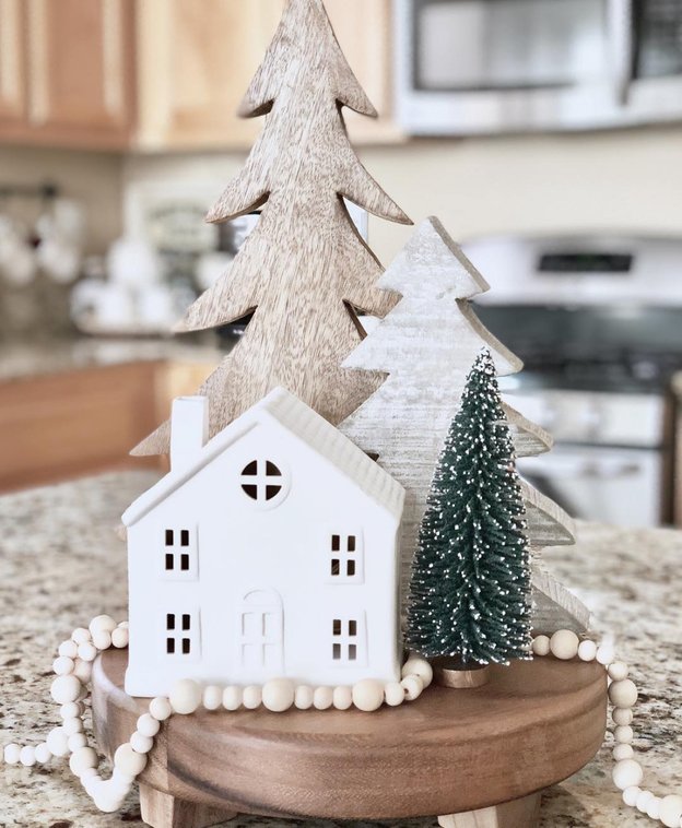 Small wooden pedestal holding a miniature Nordic village with warm string lights.