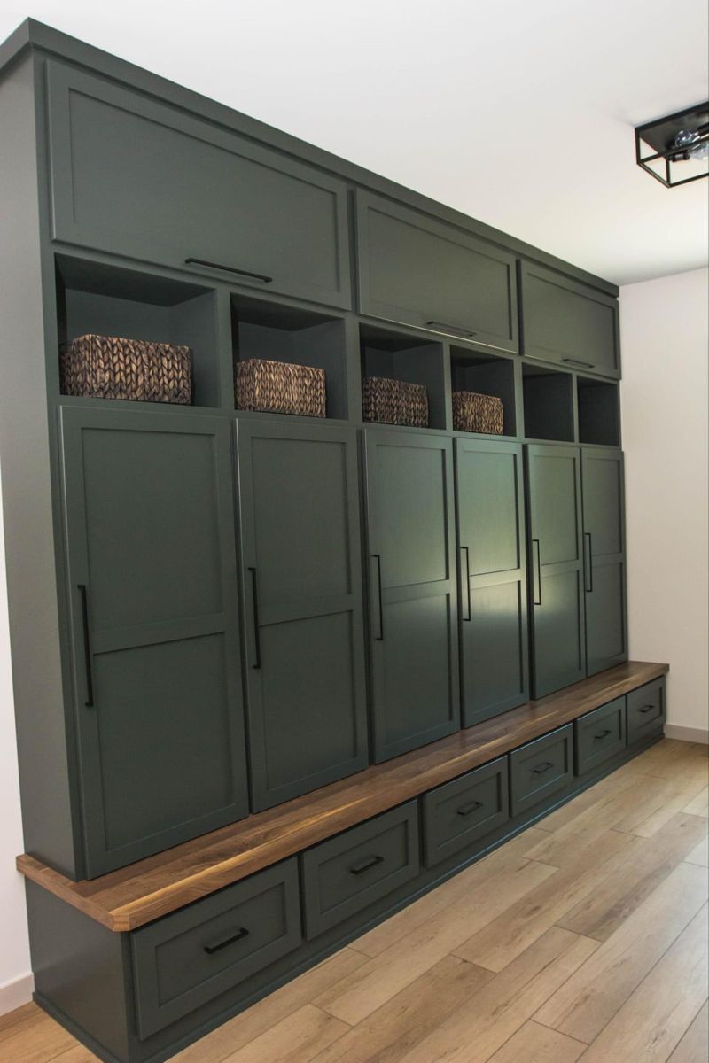 Mudroom with deep green lockers, walnut bench, brass hardware, warm ambient lighting