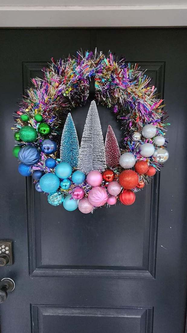 Front door, wooden entry table, rainbow baubles, natural pine wreath, warm porch lighting