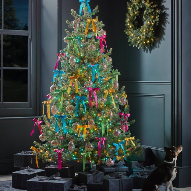 Eclectic family room tree featuring colorful jewel-tone ribbons, velvet sectional sofa, warm lighting