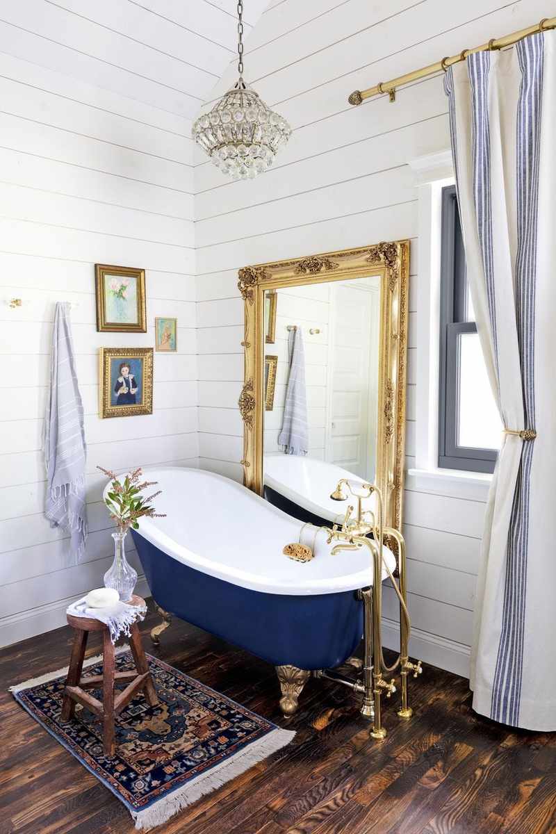 Deep navy painted clawfoot bathtub set against white horizontal shiplap walls and dark hardwood floors.