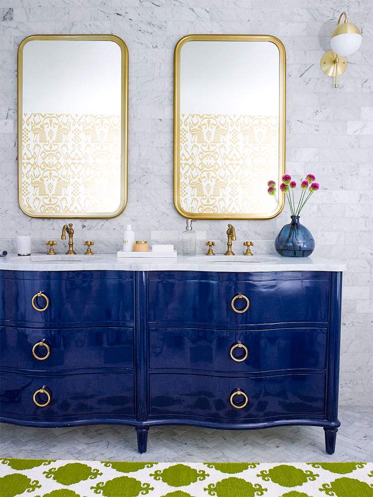 Double navy blue bathroom vanity featuring white marble counters, gold hardware, and twin brass mirrors.