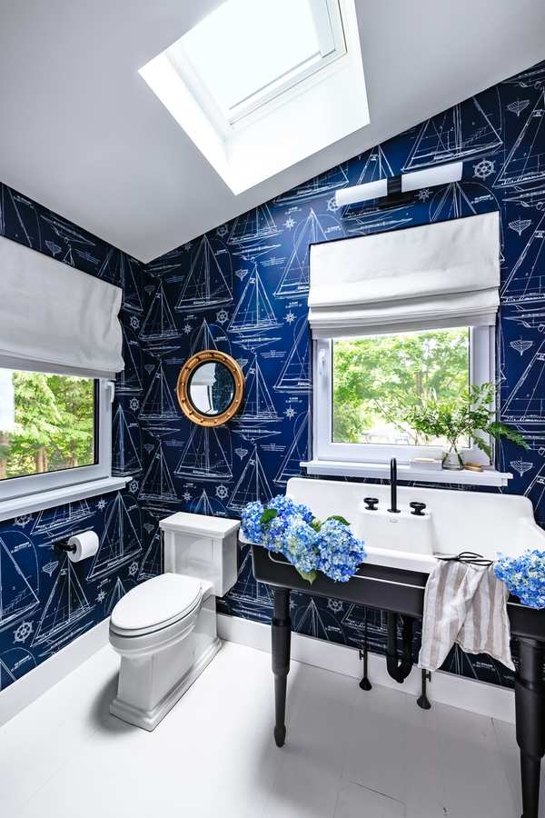 Freestanding white bathtub surrounded by dark navy floral wallpaper and brushed brass fixtures.
