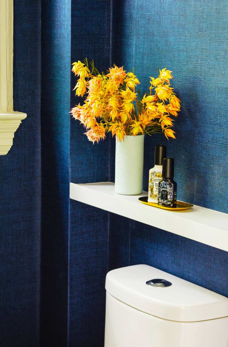 Matte navy blue bathroom walls decorated with bright yellow floral arrangements and brass fixtures.