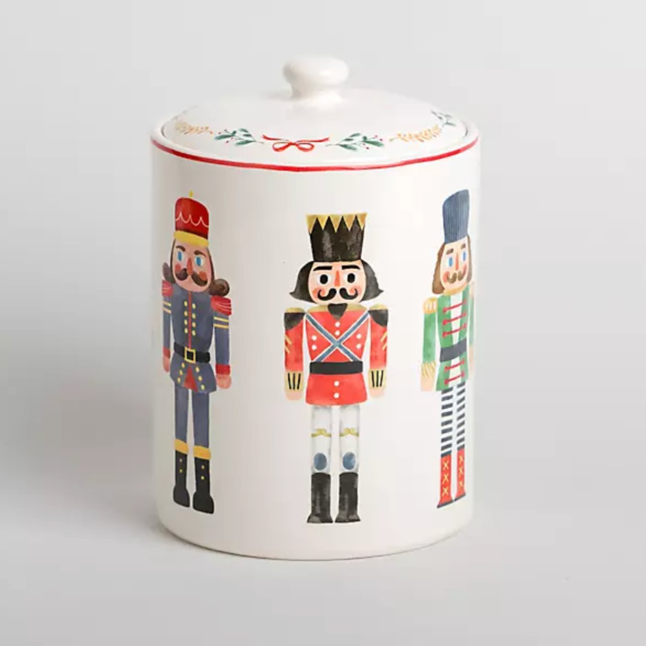 Ceramic nutcracker cookie jar with a red lid on a kitchen counter with holiday cookies.