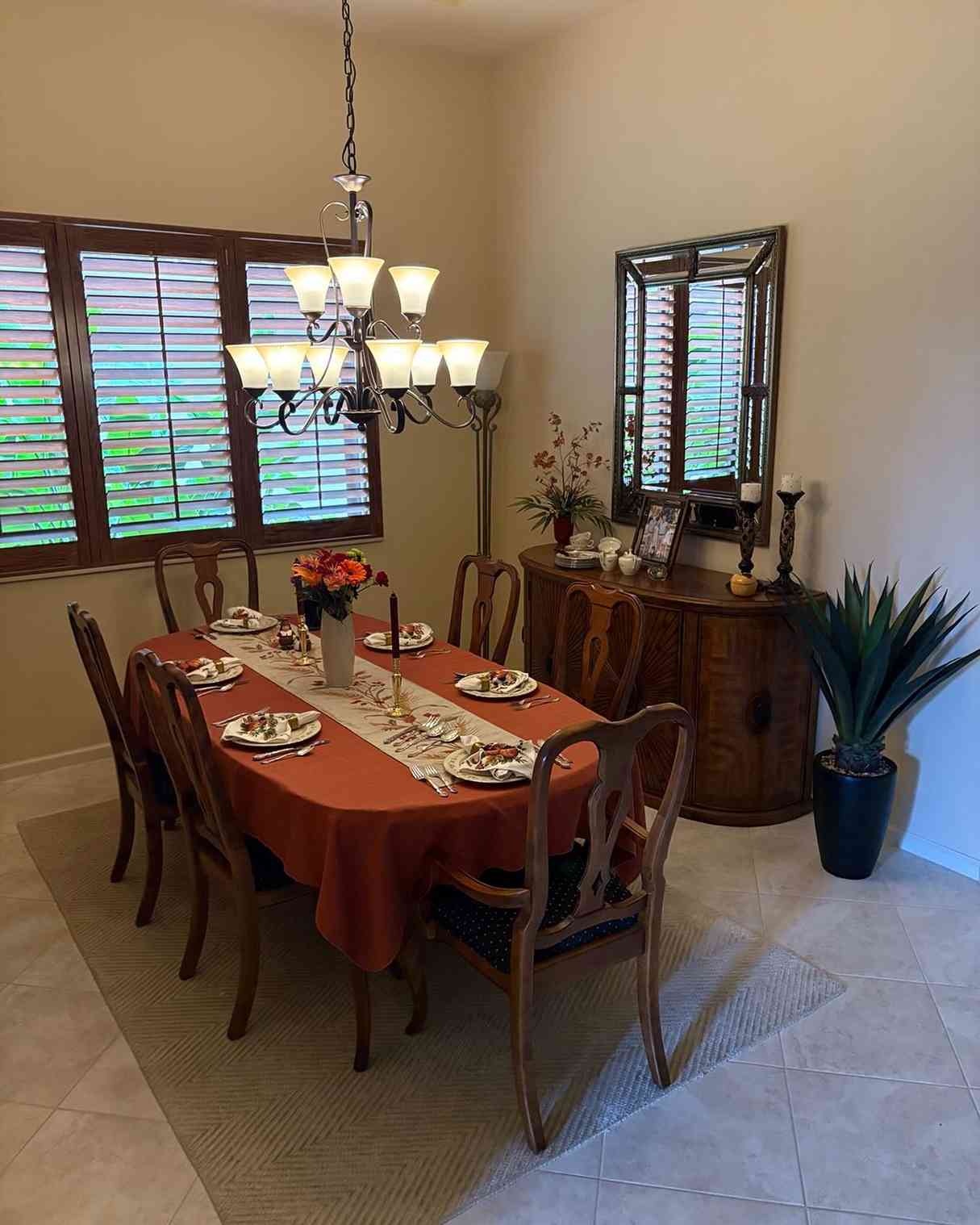 Oval dining room, rust‑colored tablecloth, wooden table, fall flower arrangement, soft ambient lighting.