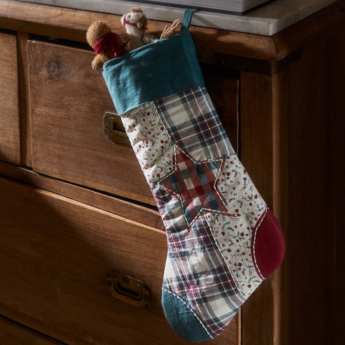 Colorful patchwork christmas stocking hanging from a mantel with a red bow.