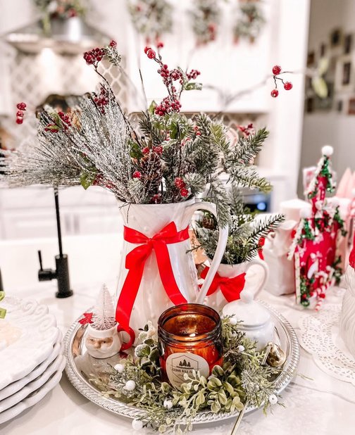 Ceramic pitcher filled with pine greenery and a large red velvet bow on counter.