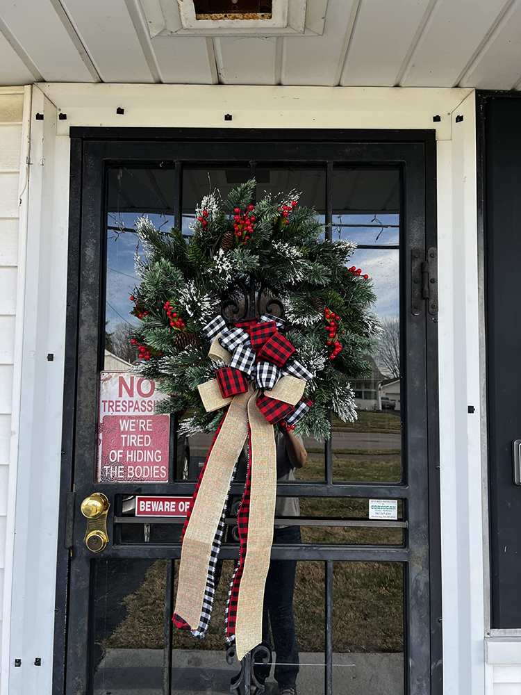 Frosted pine wreath adorned with a large red and black buffalo check plaid bow.