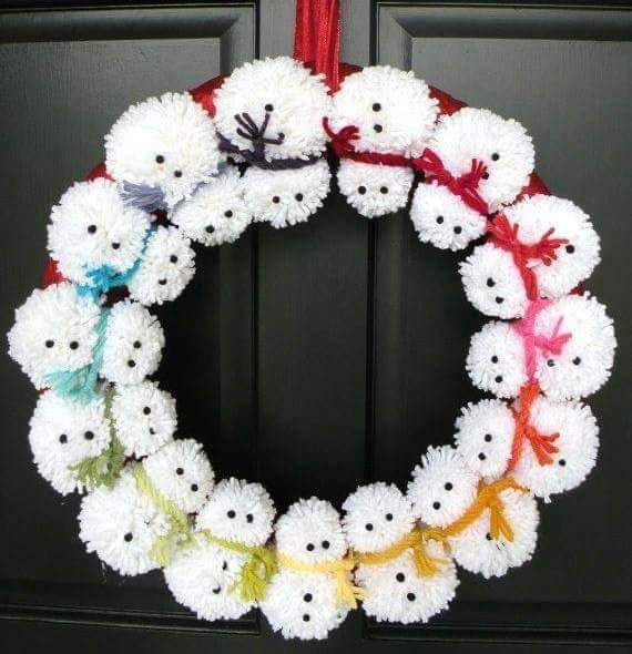 A wreath shaped like a snowman face using white yarn pom poms and festive accessories.