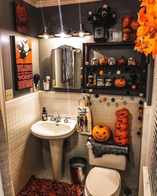 Small powder room, stacked jack‑o‑lanterns, skull shadow box, white walls, warm pendant light.