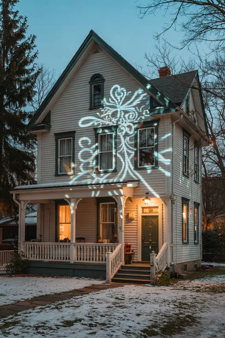 Two story stone facade illuminated with soft falling white snowflake projector lighting display.