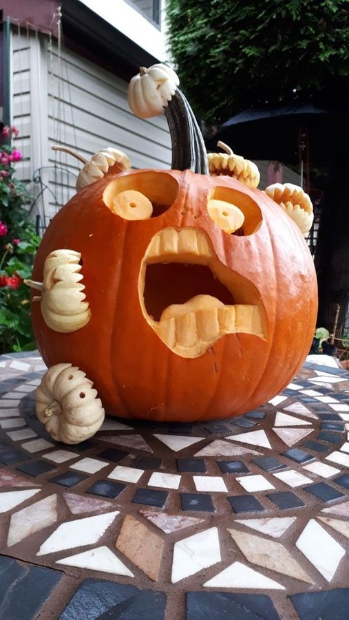 A large orange pumpkin featuring a hand-carved serif letter monogram on a wooden porch.