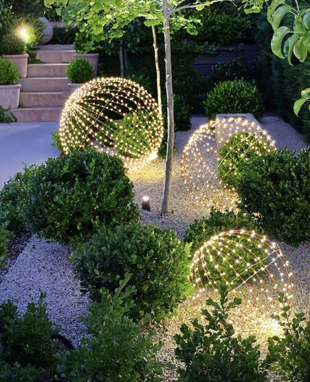Manicured winter lawn scattered with glowing woven grapevine and metal light spheres of varying sizes.