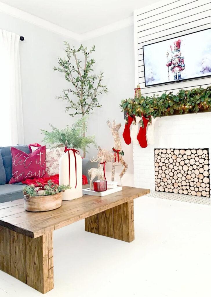 Rustic wooden coffee table decorated with bold red ornaments, cedar branches, and warm candle glow.