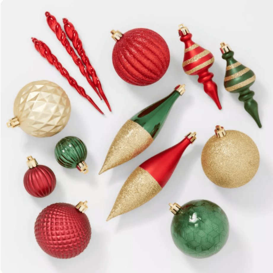 Blue, red, and green finial glass ornaments hanging on a tree branch with warm lights.