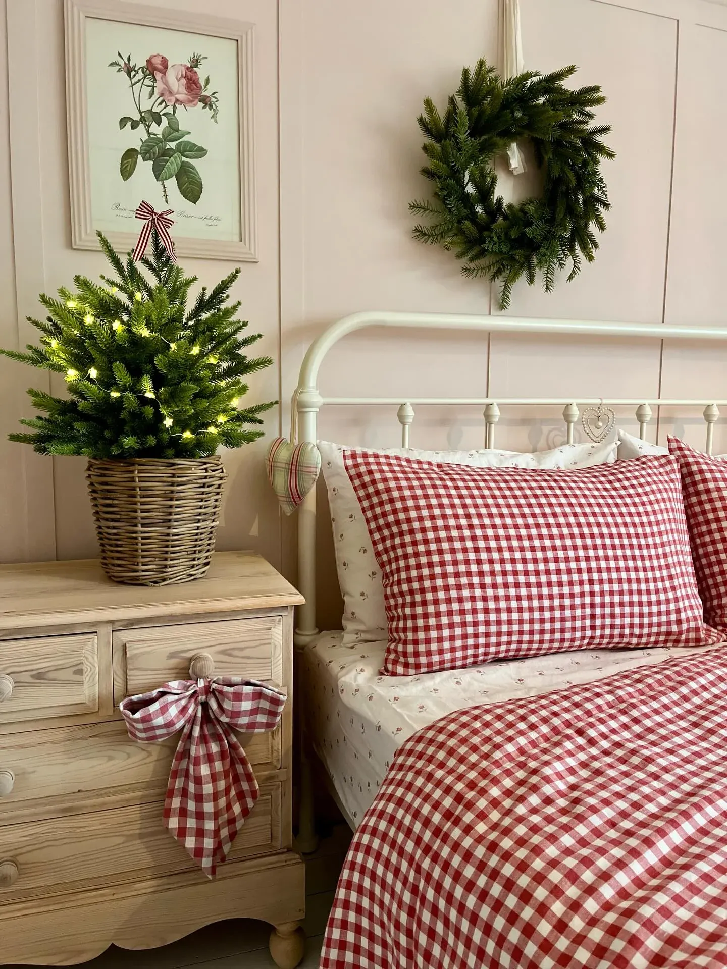 Bed with red and white plaid comforter, small Christmas tree, white walls, and festive pillows.