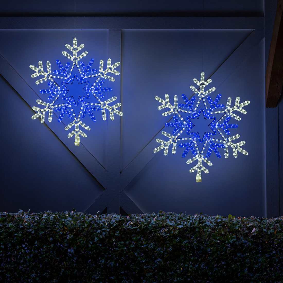 A large, glowing rope light snowflake mounted on an exterior wall as outdoor christmas decorations.