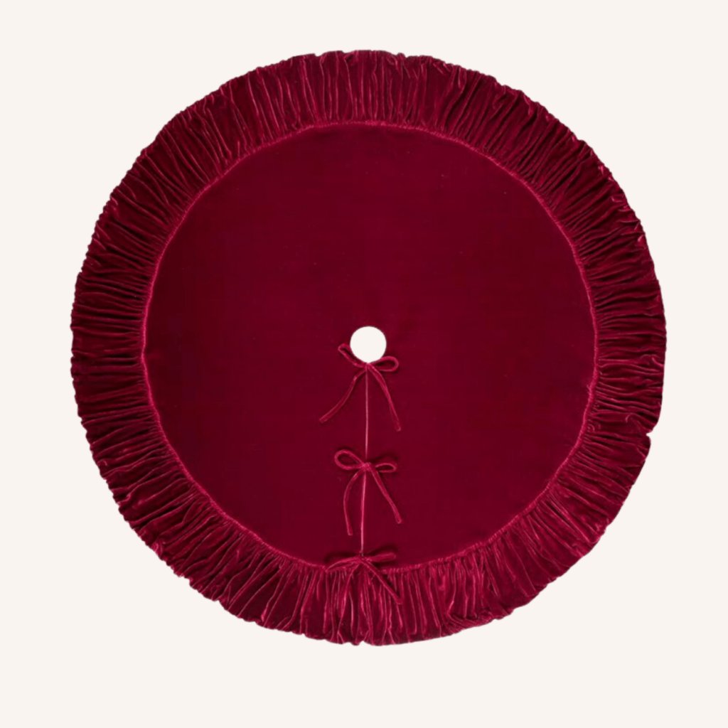 Deep red ruffled velvet tree skirt covering the base of a flocked tree in a cozy living room.