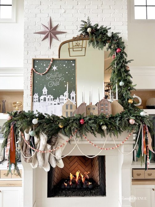 Traditional living room stone fireplace draped in layered mixed greenery garland and glowing taper candles