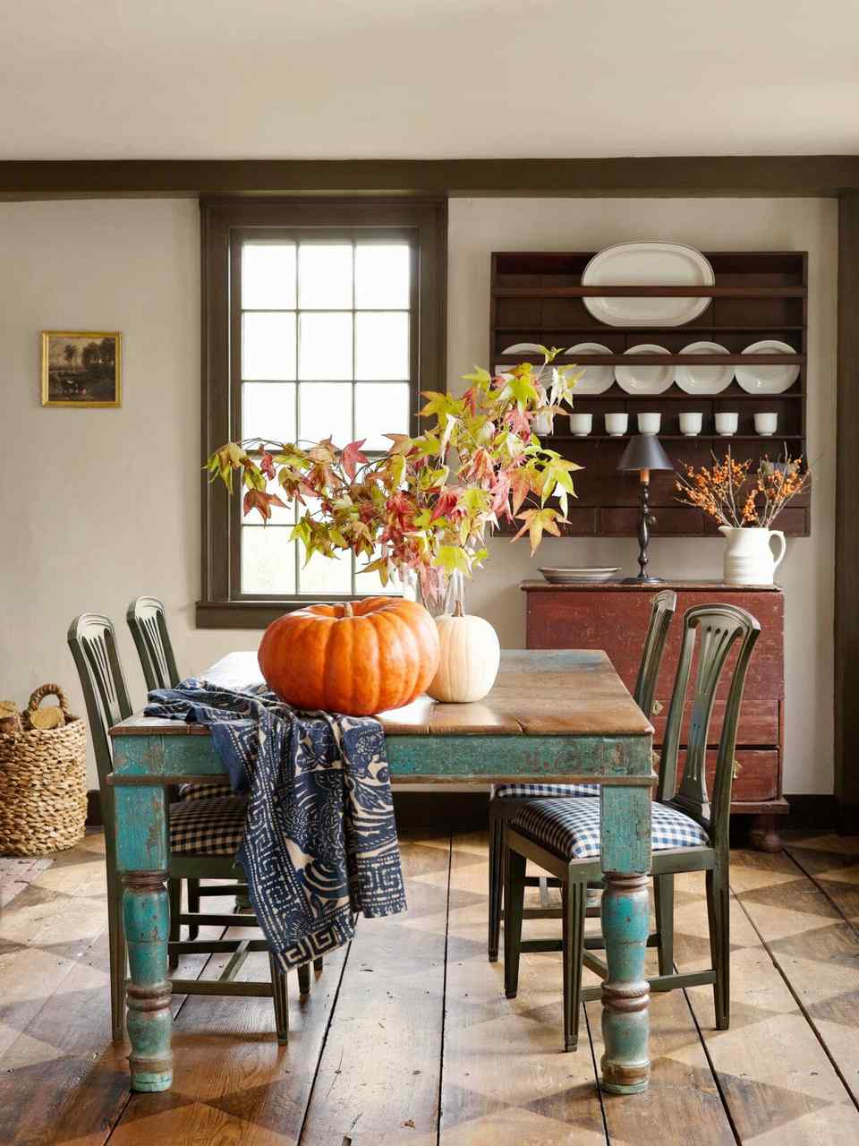 Rustic dining room, turquoise tabletop, pumpkins, autumn branches, distressed wood chairs, ambient warm lighting.