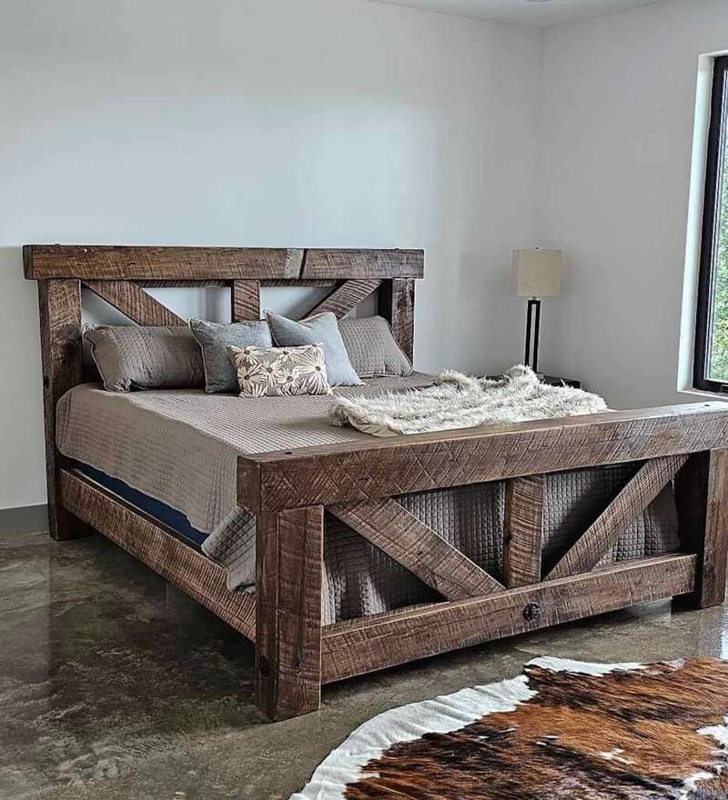 Rustic bedroom featuring a cross‑brace wooden bed frame, neutral linen bedding, and a black cowhide rug